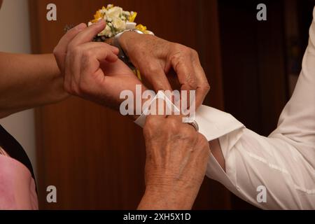 Woman is helping a groom buttoning up his white shirt cuff as he is getting ready for his wedding Stock Photo