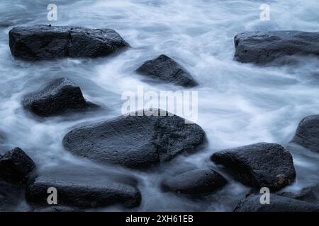 Misty water around dark moody rocks Stock Photo