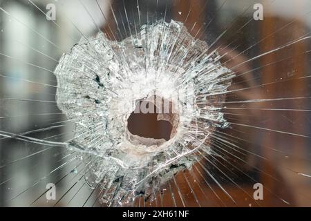 Close-up of shattered glass with a central bullet hole impact Stock Photo