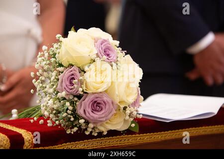 Beautiful wedding bouquet with white and purple roses lying on a red velvet cushion during a wedding ceremony Stock Photo