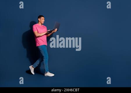 Full body length photo of young man freelancer walking using computer working remote isolated on dark blue color background Stock Photo