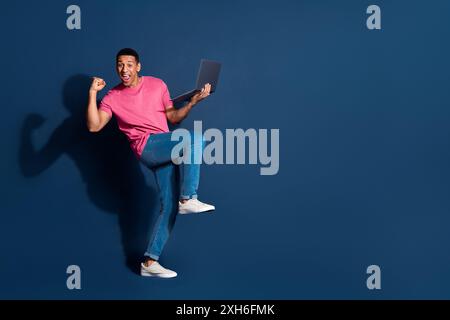 Full body length photo of young guy it developer using computer working online always gets benefits isolated on dark blue color background Stock Photo