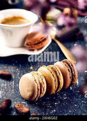 A close-up of assorted macarons shallow depth of field with a cup of coffee in the background on a dark surface Stock Photo
