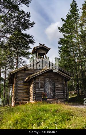 A small wooden mountain chapel stands amidst tall pine trees in the Swedish forest, a Christian cross visible on its exterior in Idre Dalarna Stock Photo