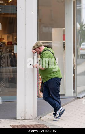 11 July 2024. Leith,Edinburgh,Scotland. This is a man using his mobile phone whilst leaning against a pillar of a shopping centre in Leith, Edinburgh Stock Photo