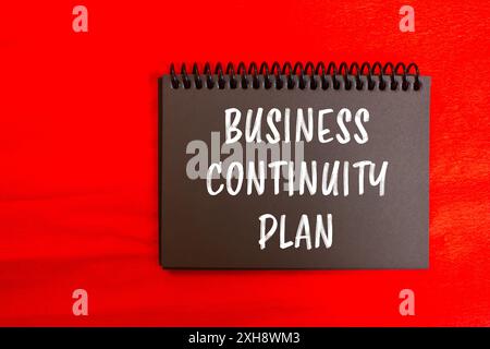 Business continuity plan message written on black notebook page with red background. Conceptual business continuity plan symbol. Copy space. Stock Photo