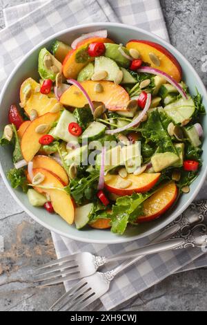 Peach avocado salad with onion, chili, arugula, spinach and pumpkin seeds close-up in a bowl on the table. Vertical top view from above Stock Photo