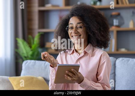 Happy student looking at camera talking and holding a notebook during virtual meeting or online learning from home Stock Photo