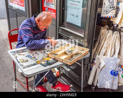Man of the street (homeless / collecting donations) assembling a jig-saw puzzle - Paris 75006, France. Stock Photo