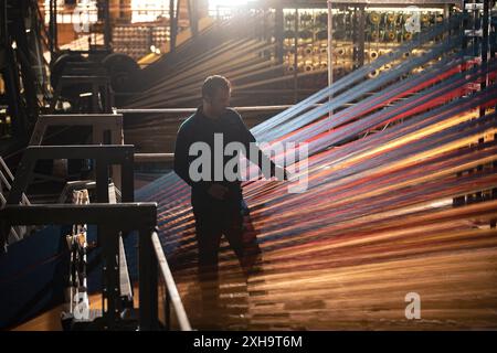 Man working on colorful yarns in a traditional weaving factory with sunlight streaming in. Stock Photo
