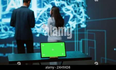 AI programmers colleagues using green screen laptop for business data analysis. IT experts in high tech location work on chroma key notebook to automatize tasks using artificial intelligence, camera A Stock Photo