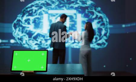AI programmers colleagues using green screen laptop for business data analysis. IT experts in high tech location work on chroma key notebook to automatize tasks using artificial intelligence, camera B Stock Photo