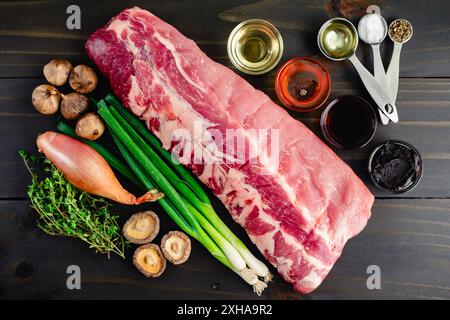 Ingredients for Pork Ribs with Black Garlic-Red Miso Sauce: Raw slab of baby back ribs, red miso, black garlic, and more on a dark wooden background Stock Photo