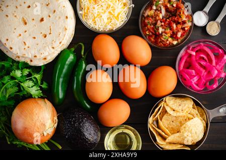 Tex-Mex Migas Breakfast Tacos Ingredients: Eggs, tortilla chips, jalapeno peppers, flour tortillas, shredded cheese, and more on a wooden table Stock Photo