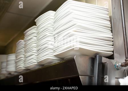 A view of several stacks of white plates on a shelf, in a restaurant kitchen setting. Stock Photo