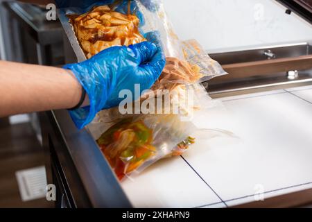 A view of a person using a vacuum packing machine, used in the industry to seal plastic bags of food. Bags of meal prep are being prepared. Stock Photo