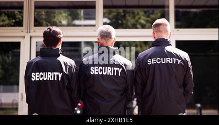 Security team of uniformed guards stand with hands clasped behind their backs in a row, safeguarding a corporate event. Stock Photo