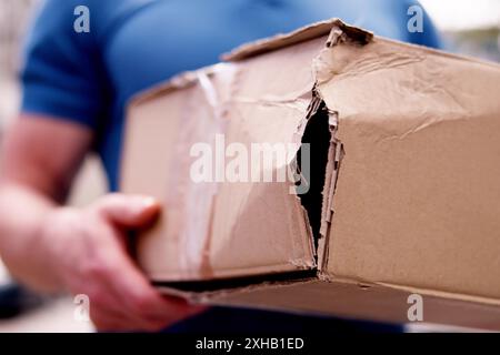 The young mailman was carefully carrying a fragile box for delivery, but a mistake led to it being damaged. Protect your items with insurance. Stock Photo