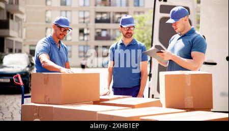 Efficient Courier Delivery and Professional Movers Near Van: A Group of Workers Unloading Boxes from Removal Truck. Stock Photo