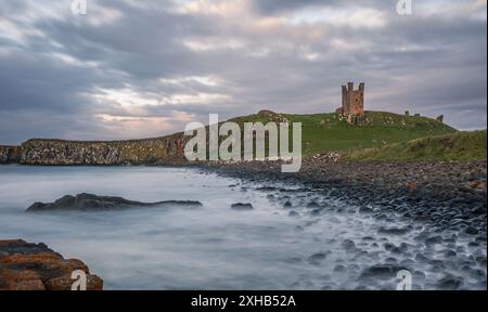 The ruins of Dunstanburgh castle ubove the black rocks of Rumble Churn at high tide, Embleton Bay Northumberland coast north east England UK Stock Photo