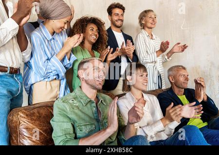 Enthusiastic diverse team clapping and cheering. Multicultural, multi-generational group showing unity and excitement in a contemporary office or even Stock Photo