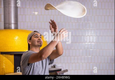 Chef tosses the pizza dough into the air. Hands of a male chef with thin round pizza dough in the kitchen.Skilled chef preparing dough for pizza rolli Stock Photo
