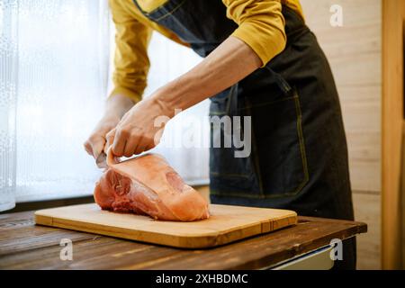 Unrecognizable man in apron cuts off skin from raw pork shoulder Stock Photo