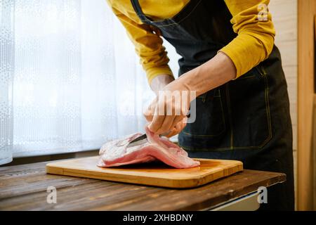 Unrecognizable man in apron cuts fat and sinews from pork shoulder meat Stock Photo