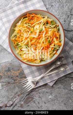 Fresh salad of white cabbage with carrots dressed with olive oil close-up in a bowl on the table. Vertical top view from above Stock Photo