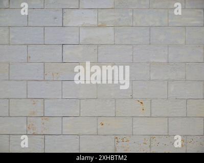 A surface wall in stretcher bond, painted white multiple times, shows paint damage, chipping, and rust spots, giving it a vintage character. Stock Photo