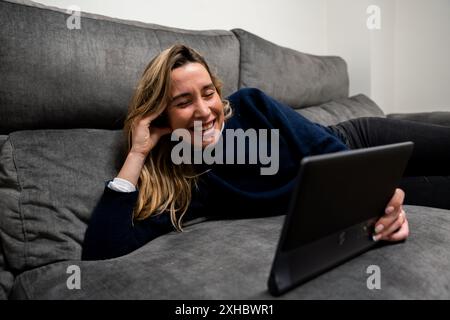 Woman lying on the sofa laughing with the tablet Stock Photo