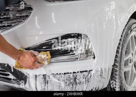 man with a sponge washes a car with foam at a car wash Stock Photo