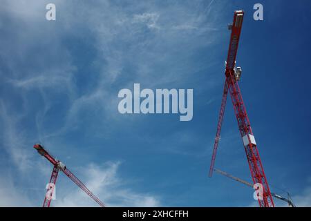 Low angle view group of three red, yellow and blue tower cranes work over building construction site against clear blue sky. Stock Photo