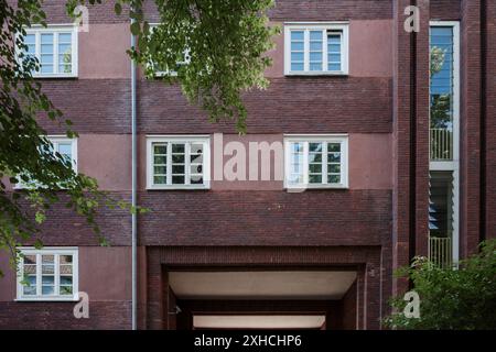 The facade of a brick building featuring symmetrical windows with white frames. The structure has alternating layers of red bricks. Stock Photo