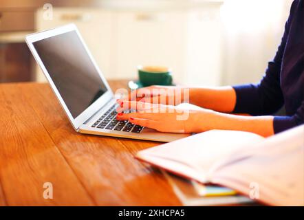 Anonymous female freelancer typing on laptop while working remotely from home at wooden table with books Stock Photo
