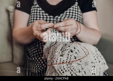 Unrecognizable crop craftswoman creating handmade knitwear while sitting on couch at home Stock Photo