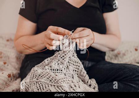 Unrecognizable crop craftswoman creating handmade knitwear while sitting on couch at home Stock Photo