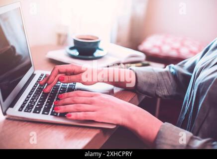 Anonymous female freelancer typing on laptop while working remotely from home at wooden table with books Stock Photo