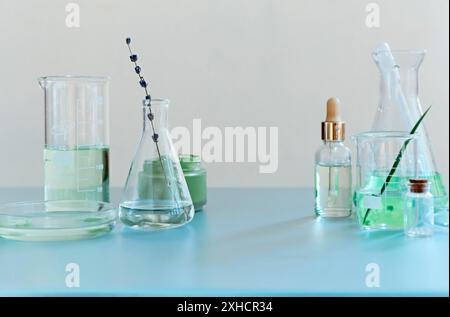 Assorted glass bottles and flasks arranged with green plants on table in modern lab Stock Photo