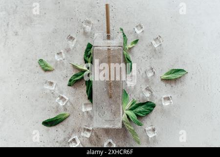 Top view of glass container with clean water and straw placed near mint leaves on gray stone surface Stock Photo