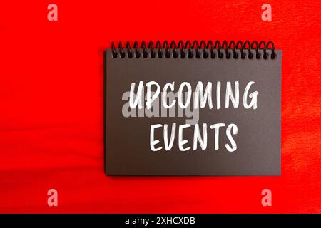 Upcoming events message written on black notebook page with red background. Conceptual upcoming events symbol. Copy space. Stock Photo