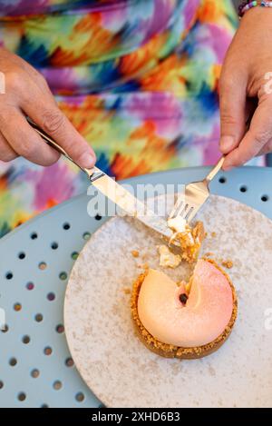 Unrecognizable female hands hold a knife and fork over a plate with peach cake dessert. Stock Photo