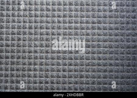 Close up of a gray door mat showing a symmetrical waffle pattern. Stock Photo