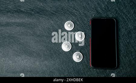 Jurmala, Latvia 25.06.2024: On a black table lies an iPhone 14 Pro Max and next to it four new airtags to plug in.  Stock Photo