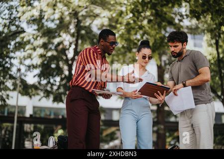 Diverse team collaborating on project in outdoor setting, discussing documents and sharing ideas Stock Photo
