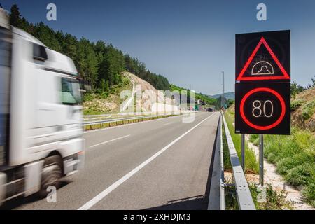 A white truck drives past a speed limit sign on a highway. The sign indicates a speed limit of 80 kilometers per hour. Stock Photo