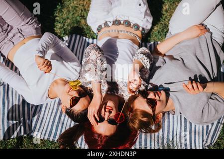 Three young women enjoying sunny day with lollipops in the park, lying on a blanket Stock Photo