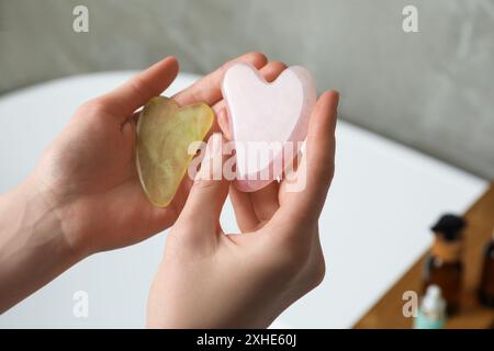 Woman holding jade and rose quartz gua sha tools in bathroom, closeup Stock Photo
