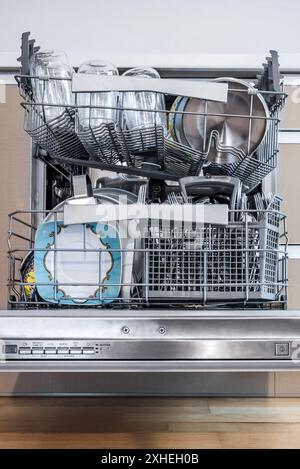 Open Dishwasher Full Of Plates, Cutlery, Glasses And Other Kitchen Dishes. Front View Stock Photo