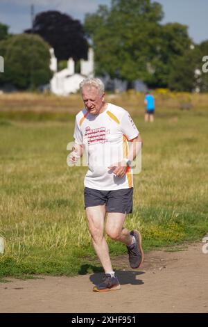 Wimbledon, London, UK. 14 July 2024  A jogger running in the bright morning sunshine on Wimbledon Common, south West London  as  forecasters predict warmer weather with highs 20Cs  around London and the South EastCredit: Amer Ghazzal/Alamy Live News Stock Photo